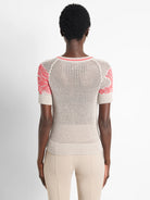 Beige mesh short-sleeved sweater with coral accents at neckline and sleeves.  Back view.