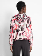 Hooded windbreaker with an abstract print.  Colors: off-white base, dark gray, black brushstrokes, and bright pink/coral...