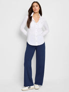 White long-sleeved button-down shirt with breast pocket; model also wears dark navy pants and white sneakers.