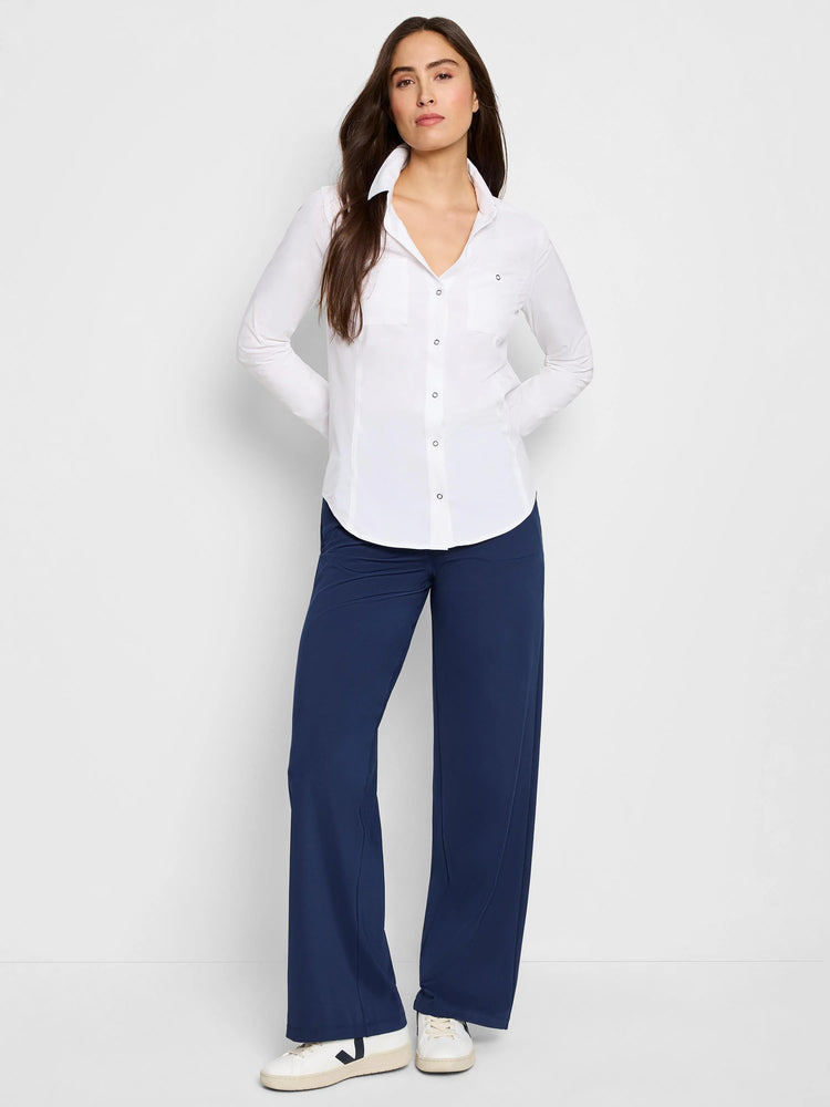 White long-sleeved button-down shirt with breast pocket; model also wears dark navy pants and white sneakers.