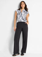 White sleeveless top with black abstract print, black wide-leg pants, black and white sneakers.