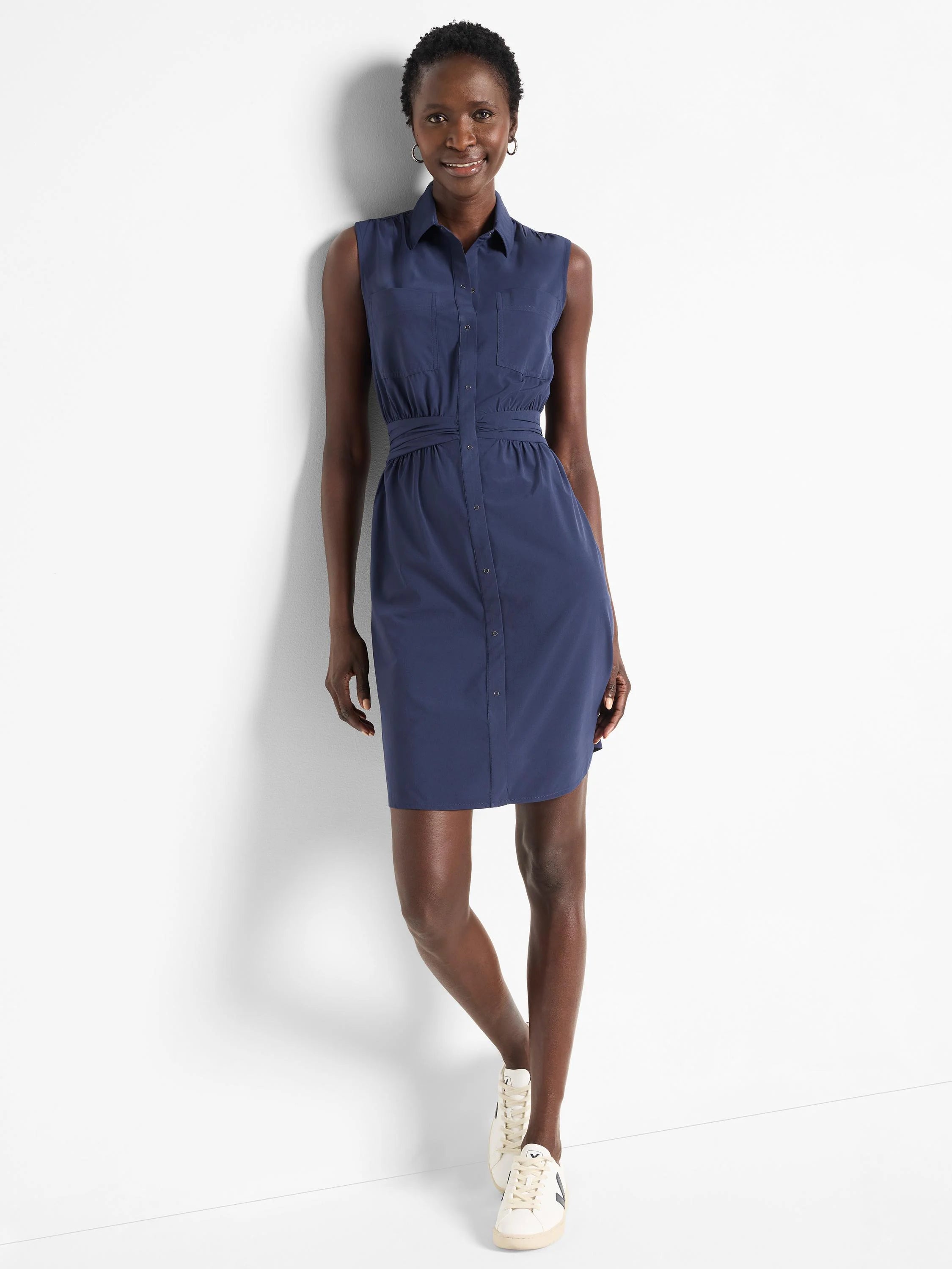 Navy blue sleeveless shirt dress with buttons, pockets, and a cinched waist.  Knee-length.