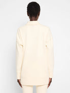 Off-white tunic with funnel neck and long sleeves; seams visible.  Back view.