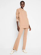 Beige tunic with funnel neck, long sleeves, and a kangaroo pocket.  Matching pants are flared.