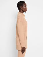 Beige tunic with funnel neck, long sleeves, and a side pocket.  Seams are visible.
