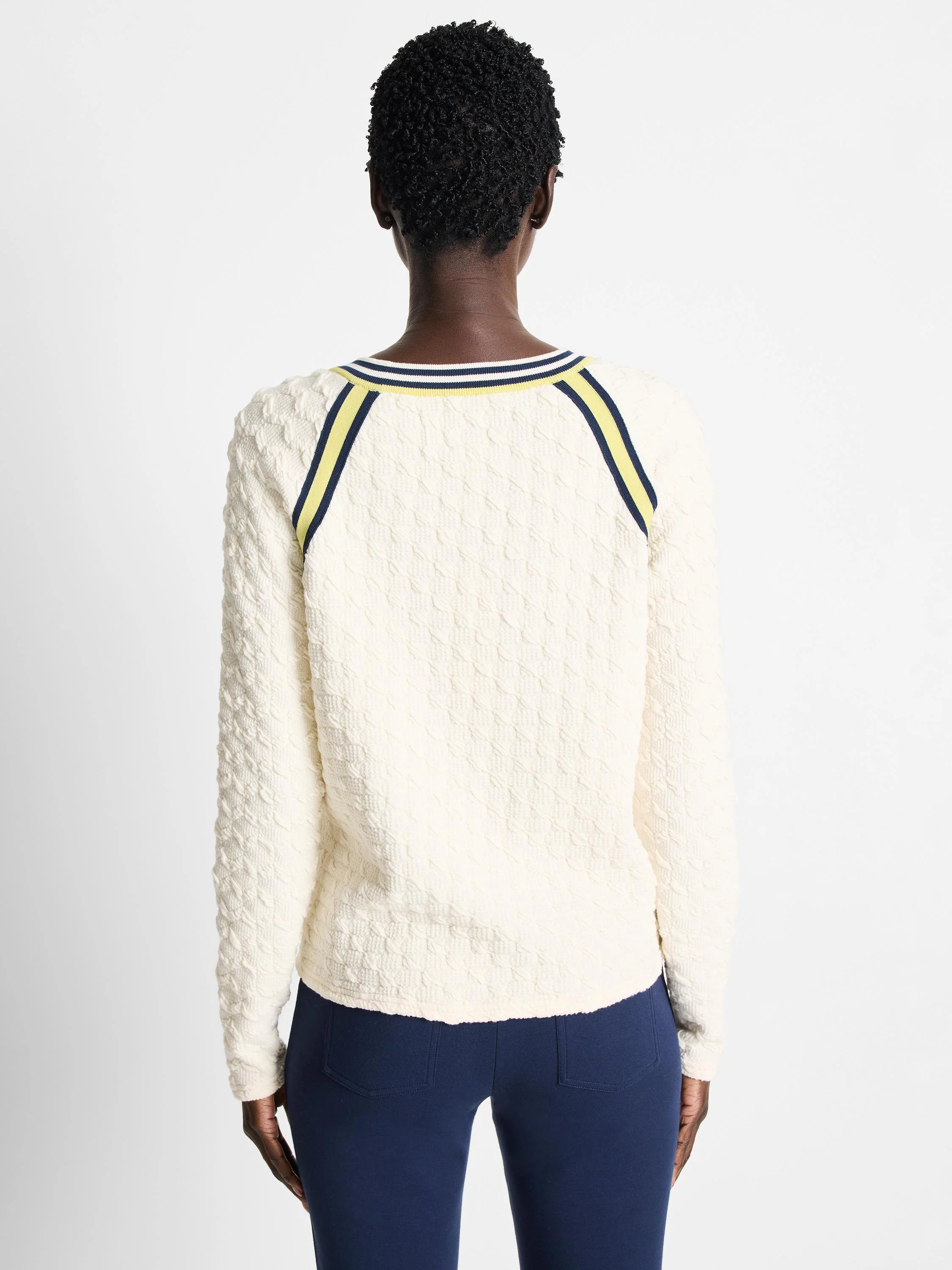 Off-white textured sweater with navy and pale yellow stripes at neckline and shoulders. Long sleeves.