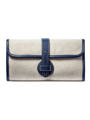 Natural linen clutch with navy blue leather trim, central strap & oval loop closure. White stitching.