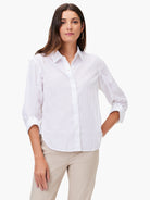 White collared button-up shirt with sleeves rolled up, crinkled texture. Worn by a woman with light beige pants.