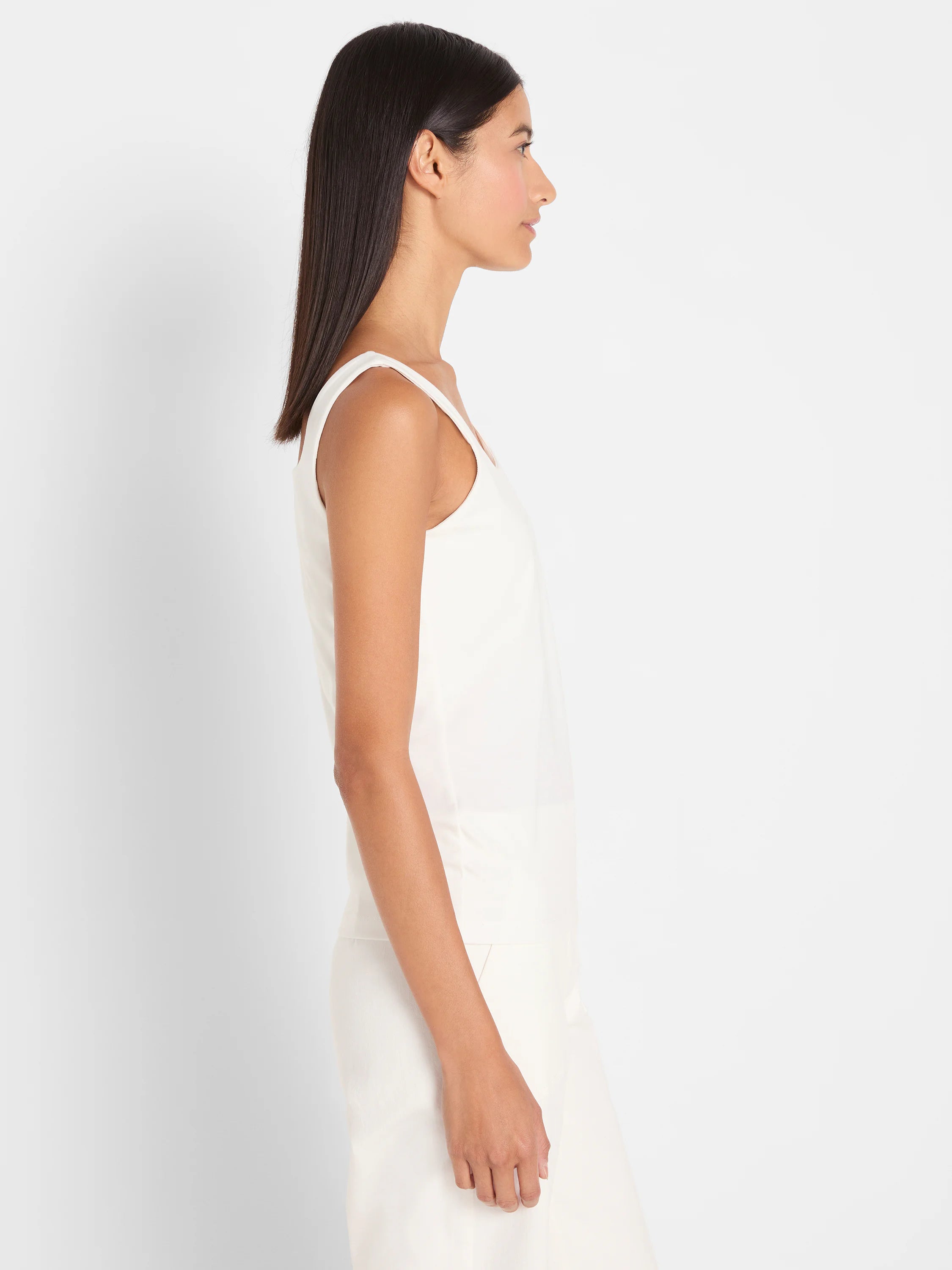 Cream tank top with wide straps on a model in profile, showing its relaxed fit.