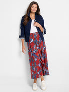 A model wears a dark denim jacket and a full red midi skirt with a bold blue and white leaf print, styled casually.