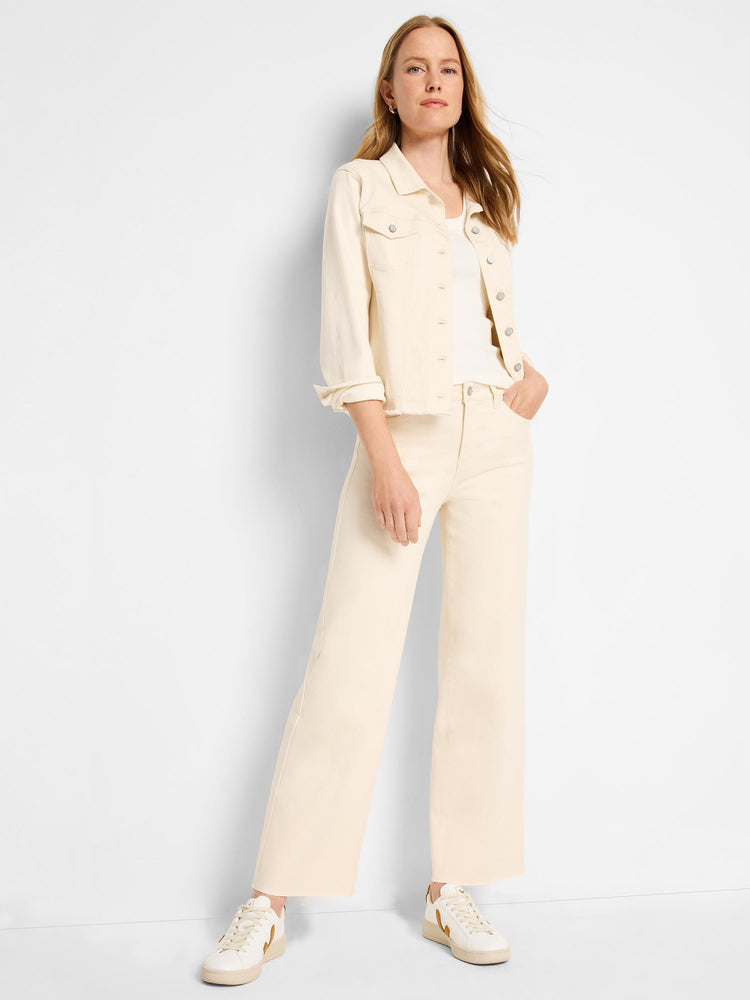 Model wearing an ecru denim jacket and matching pants. The jacket is cropped, fits relaxed, and features button closures, flap chest pockets, and raw frayed edges at the hem. The pants are high-waisted, wide-leg, and full length with raw frayed hems.