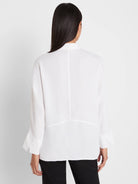 White loose-fitting blouse, back view. Features vertical back seam, horizontal seam detail, and wide cuffs.