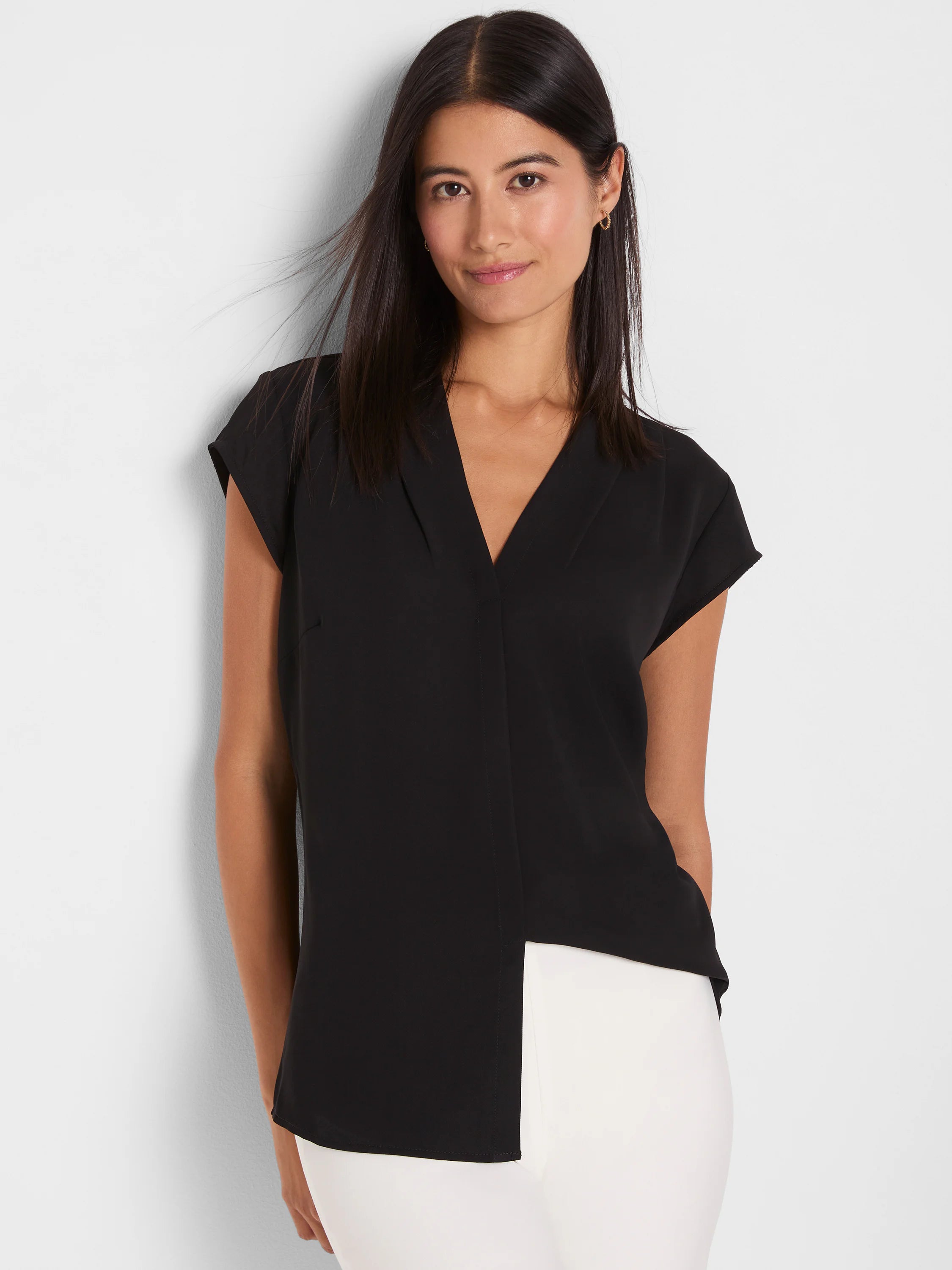 Black cap sleeve V-neck top with an overlapping front. Model wears it with white pants.