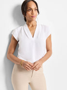 White cap sleeve V-neck top with a center front pleat, worn by a woman with beige pants.