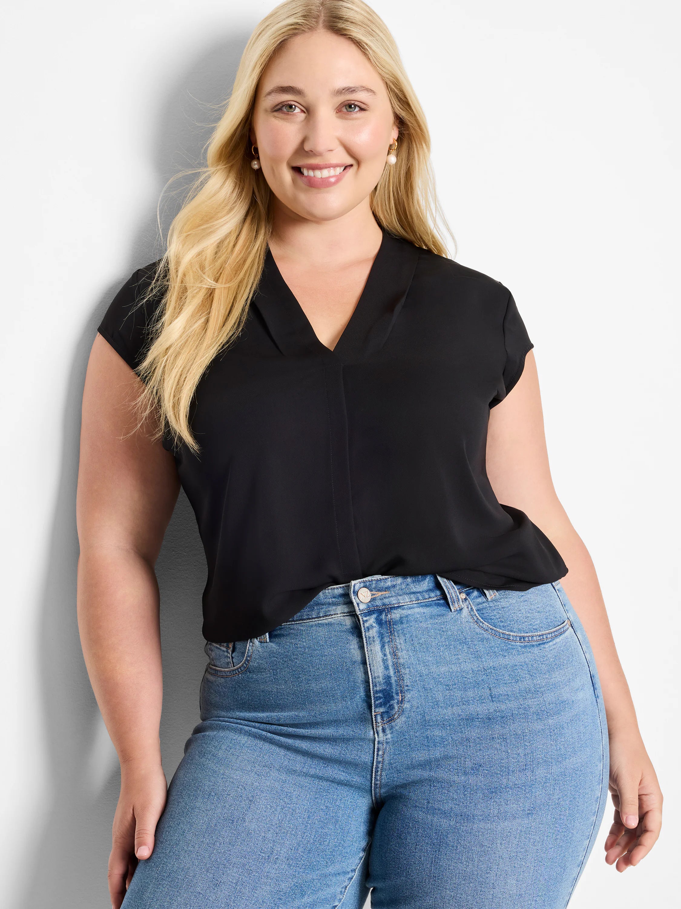 Black cap-sleeve top with V-neckline, worn with light blue jeans.