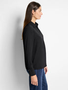 Black popover shirt with a pointed collar, V-neck placket, and long sleeves with buttoned cuffs.