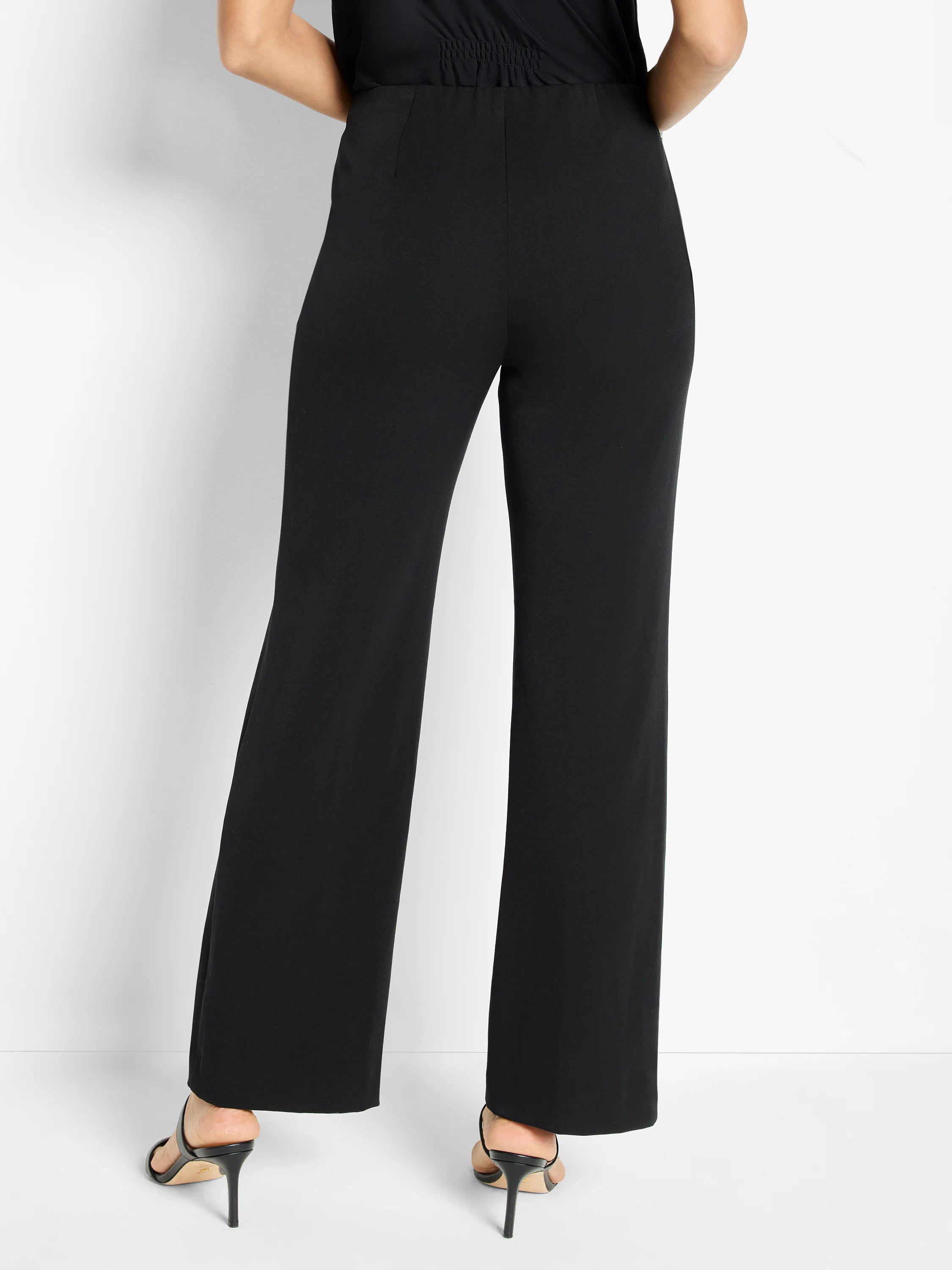 Black wide-leg trousers on a model, viewed from behind. Smooth waistband and loose-fitting legs.