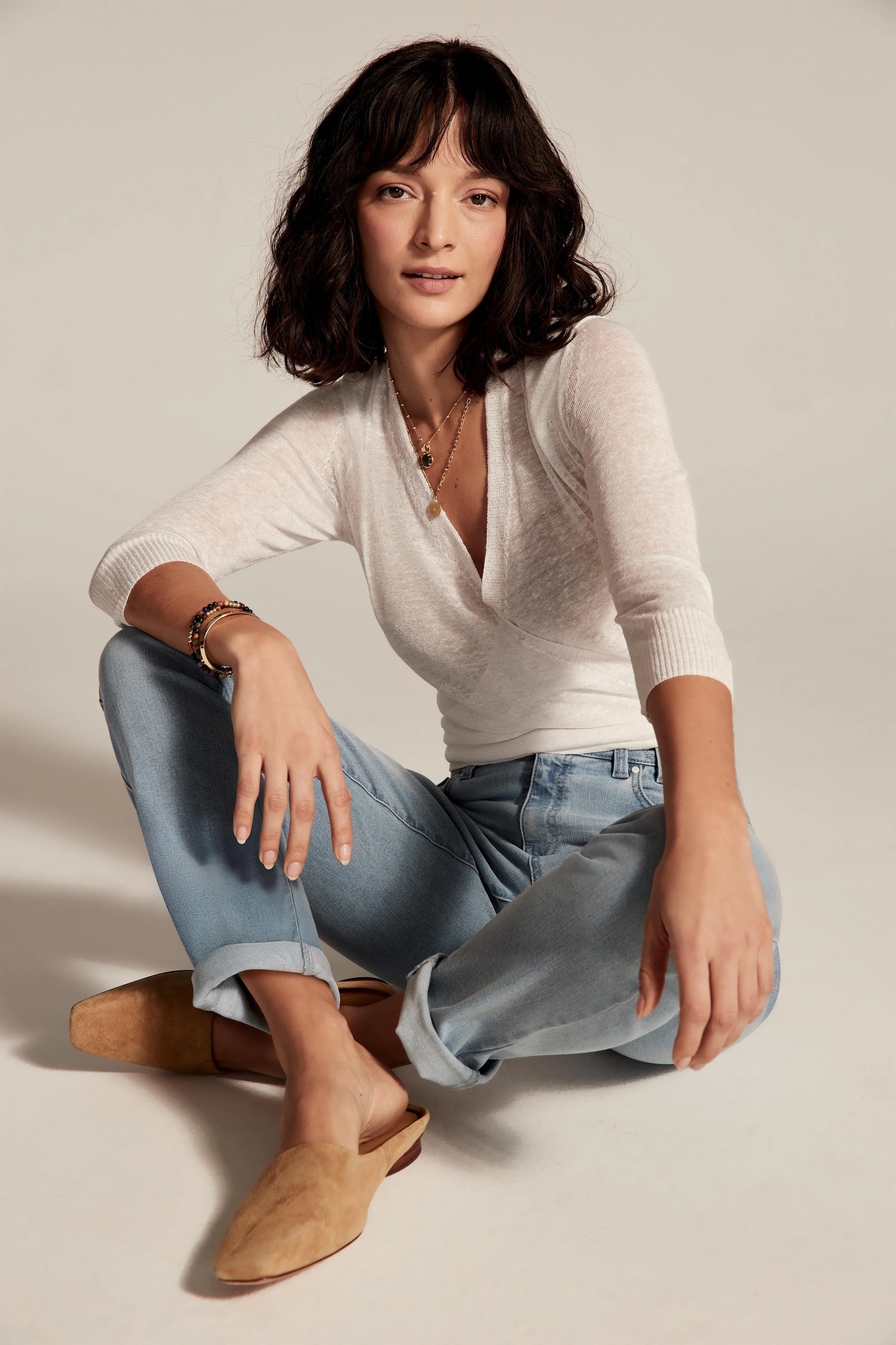 Light blue wash girlfriend jeans, mid-rise, cuffed at ankles. Model wears them sitting cross-legged.