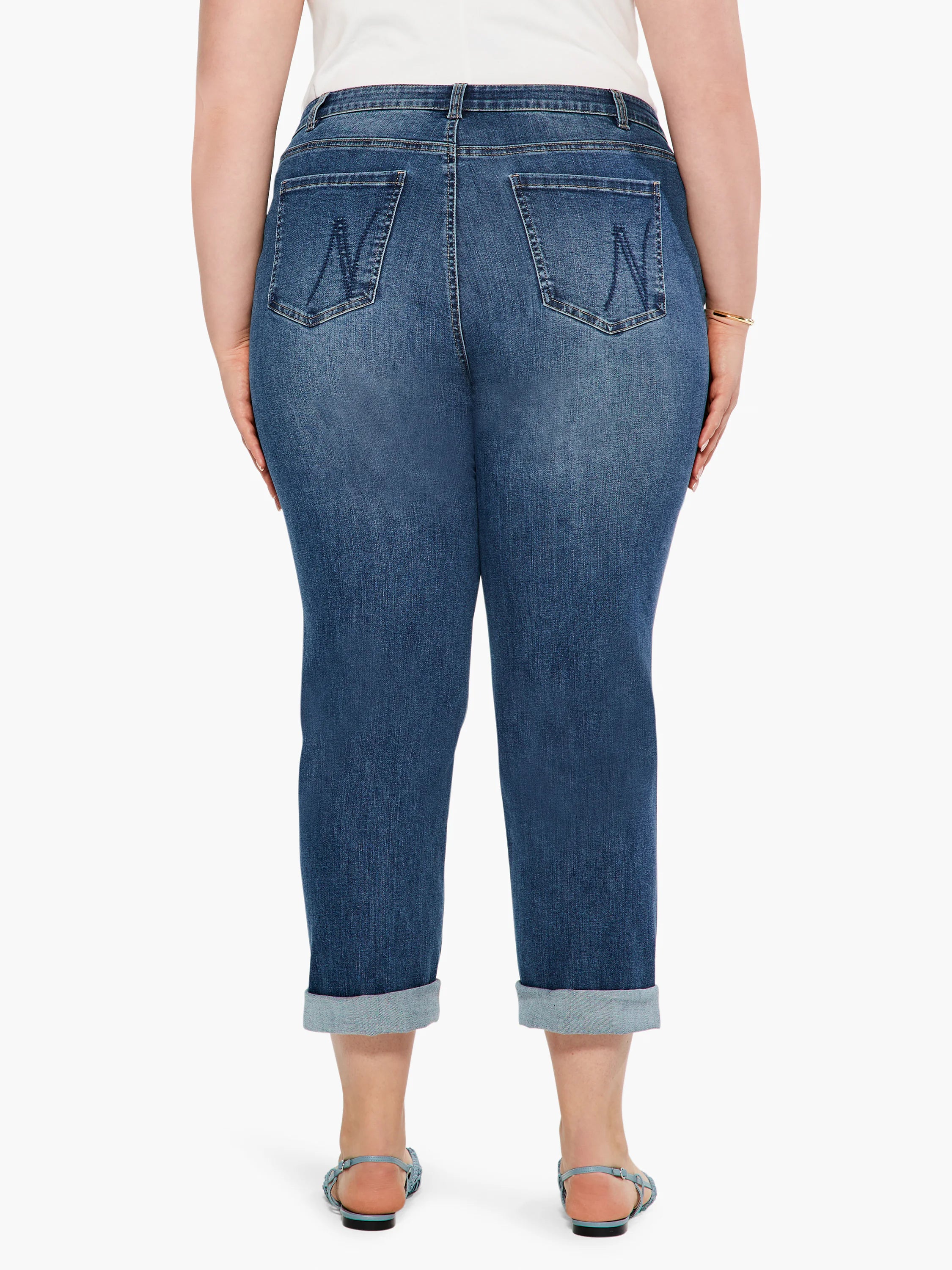 Medium blue girlfriend jeans, mid-rise, with faded areas, stylized back pockets, and cuffed ankles.