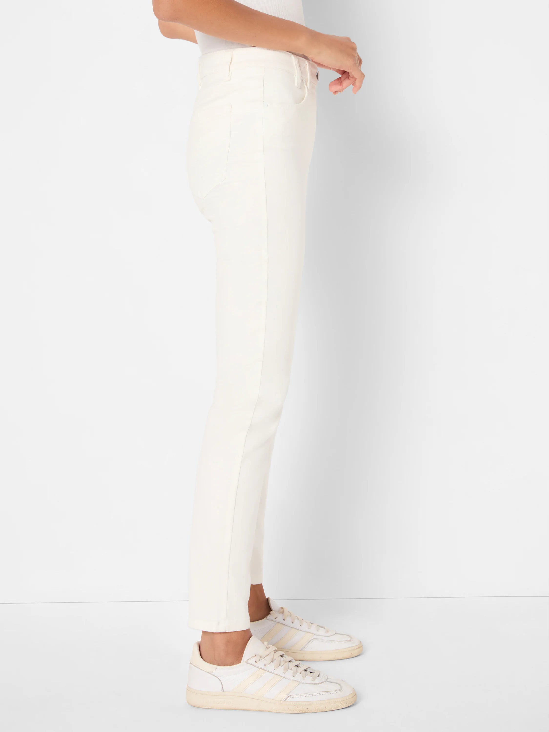 Off-white slim ankle jeans, side view. Features belt loops, front pockets with metal rivets. Ends at ankle.