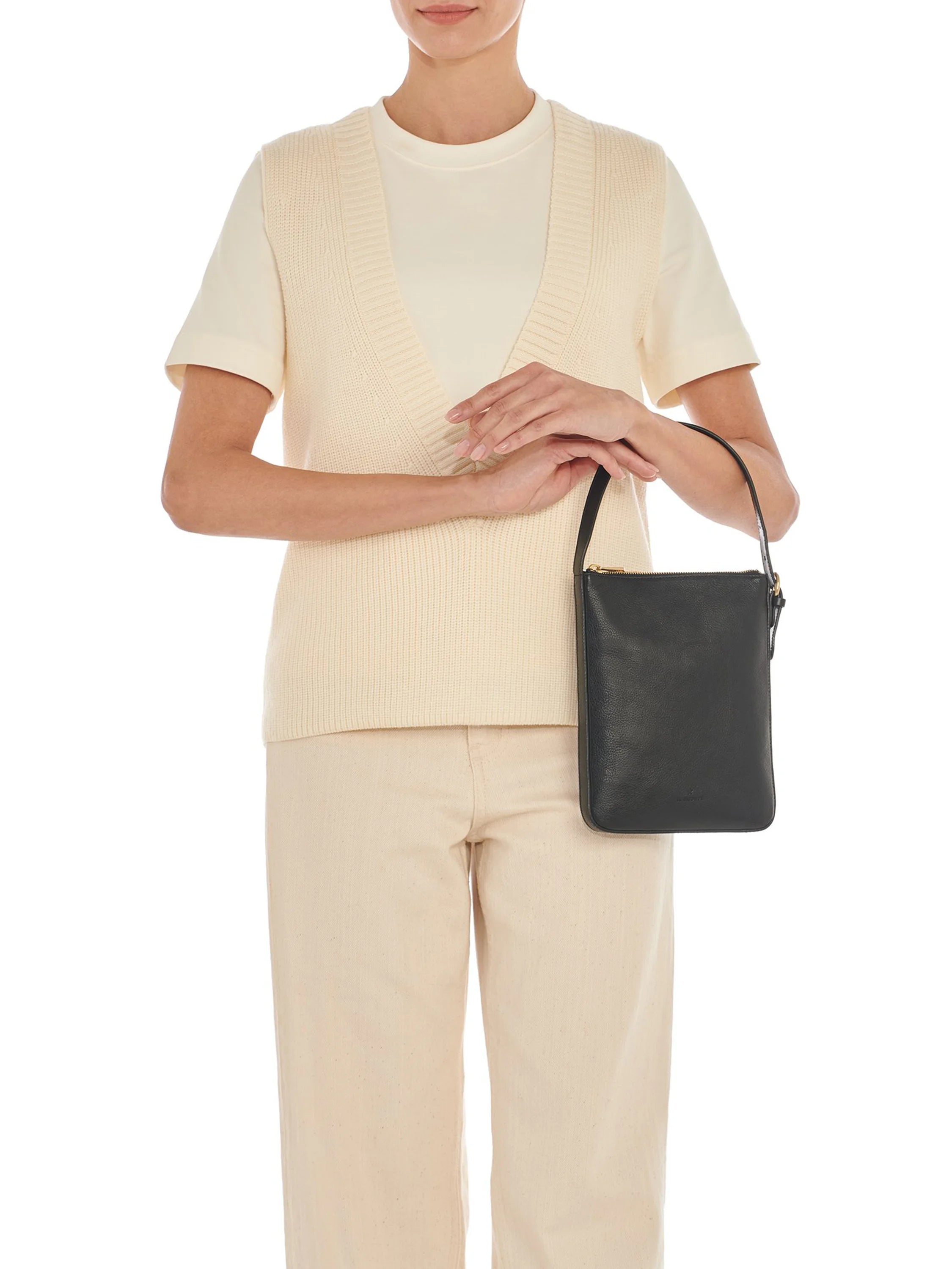 Black rectangular crossbody bag with a gold zipper, shown against a cream-colored outfit.