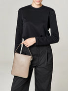 Beige rectangular crossbody bag with a top handle and zipper.  Subtle branding.