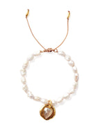 Irregular white pearl bracelet on a beige adjustable cord. Features a gold disc charm with a faceted pale stone.