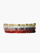 Seven layered bracelets with gold accents. Beads are red, purple, blue, green, and beige.