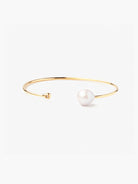 Gold cuff bracelet featuring a large off-white pearl and small clear gemstone.