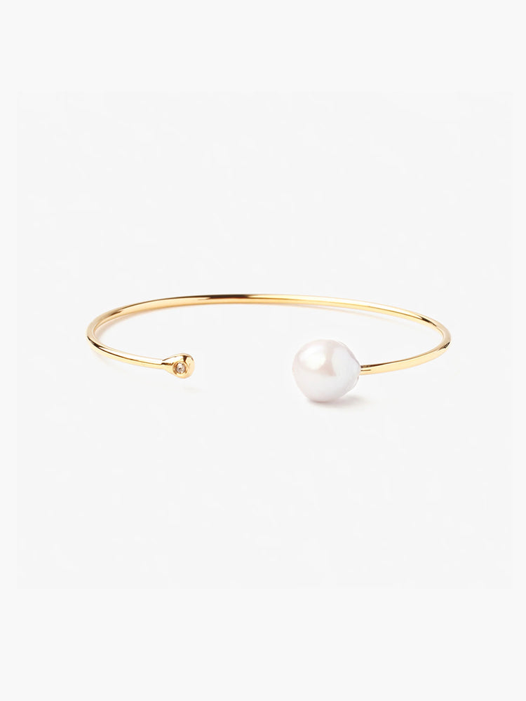 Gold cuff bracelet featuring a large off-white pearl and small clear gemstone.