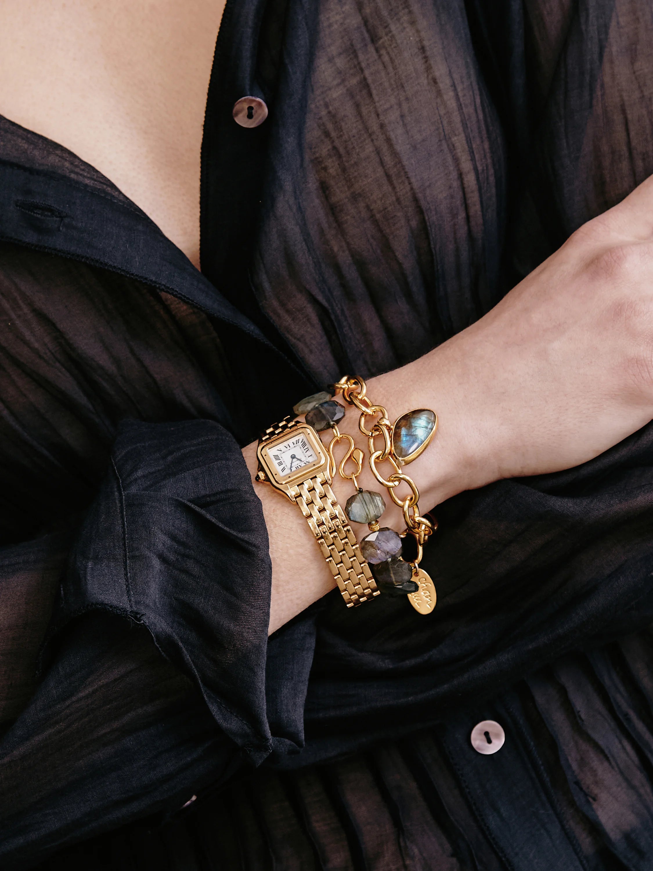 Gold chain bracelet with dark gray/blue labradorite stones and charms.