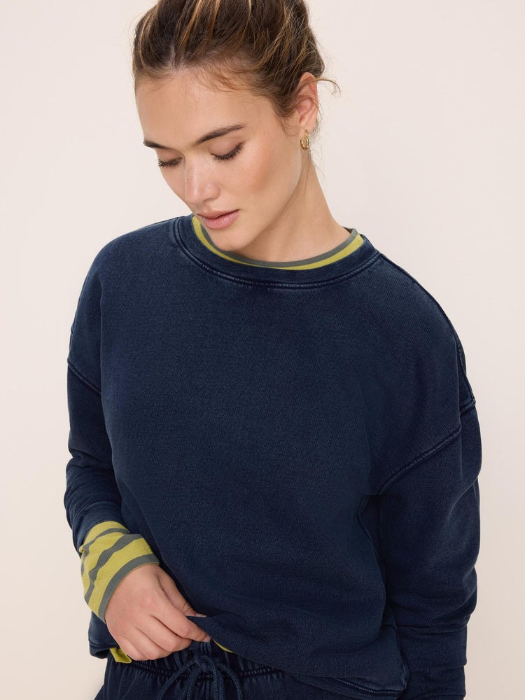 Navy cotton terry crewneck sweatshirt. A striped yellow and grey long-sleeve shirt is visible at the neck and cuffs.