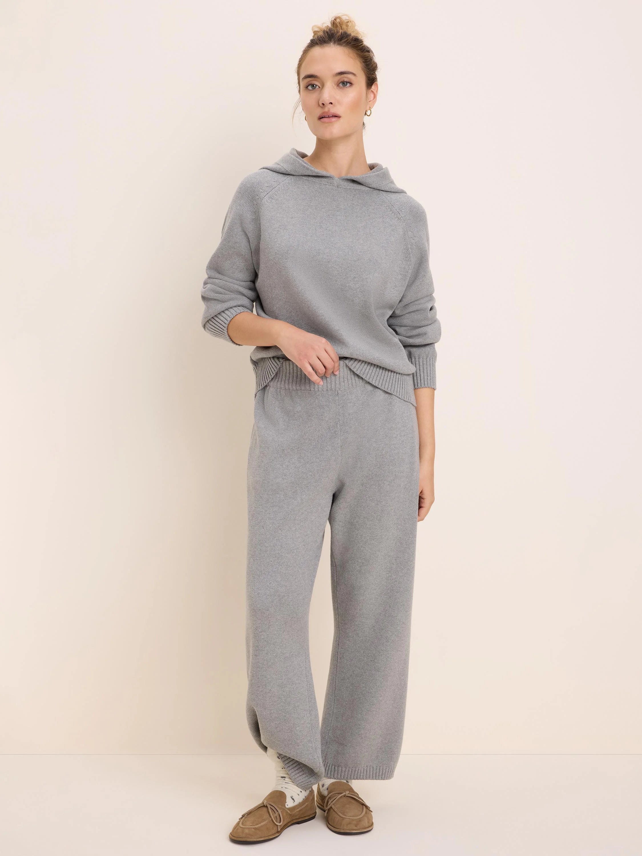 Light gray knitted sweater hoodie with ribbed cuffs and hem, modeled with matching wide-leg pants.