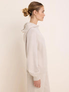 Light beige knit sweater hoodie with a hood and ribbed cuffs and hem, shown on a model in profile.