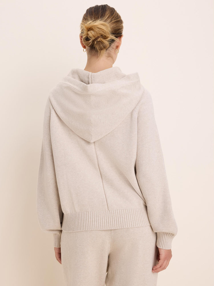 Loose-fitting light beige knit sweater hoodie with a hood, ribbed cuffs, and hem. Model shown from the back.