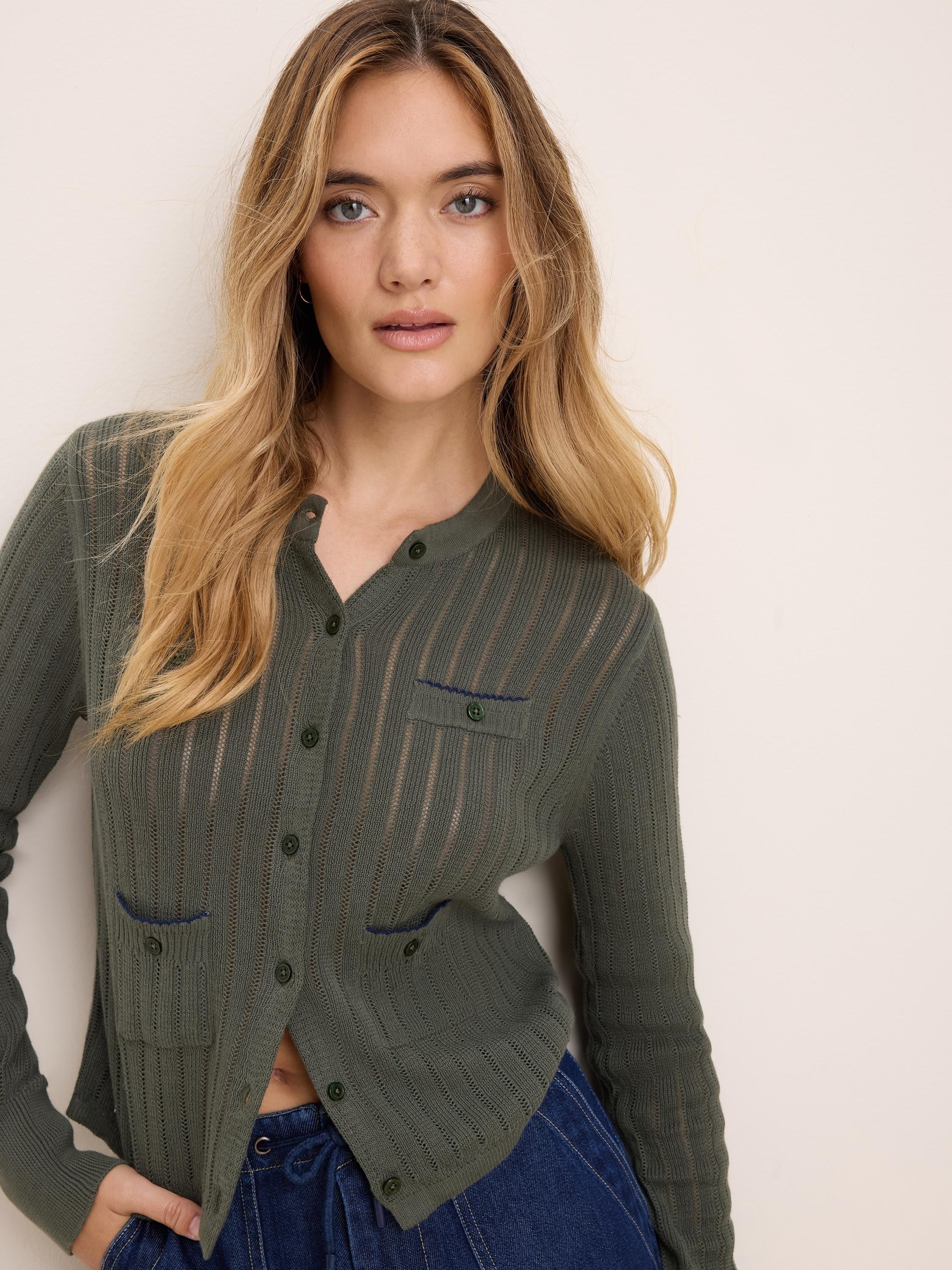 Olive green pointelle knit cardigan with button front and two blue-trimmed chest pockets.