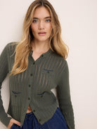 Olive green pointelle knit cardigan with button front and two blue-trimmed chest pockets.