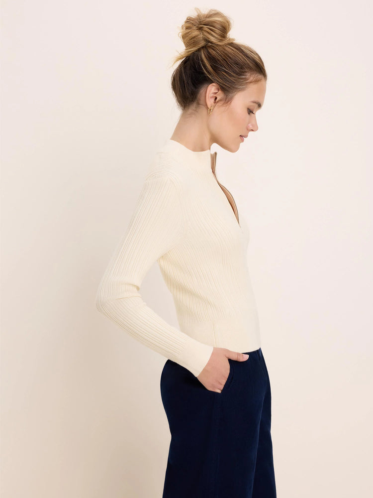 Cream ribbed half-zip sweater with a gold zipper partially open, mock neck.