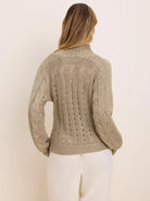 Tan cable knit cardigan on model's back, with cable patterns on sleeves and an openwork design on the back.