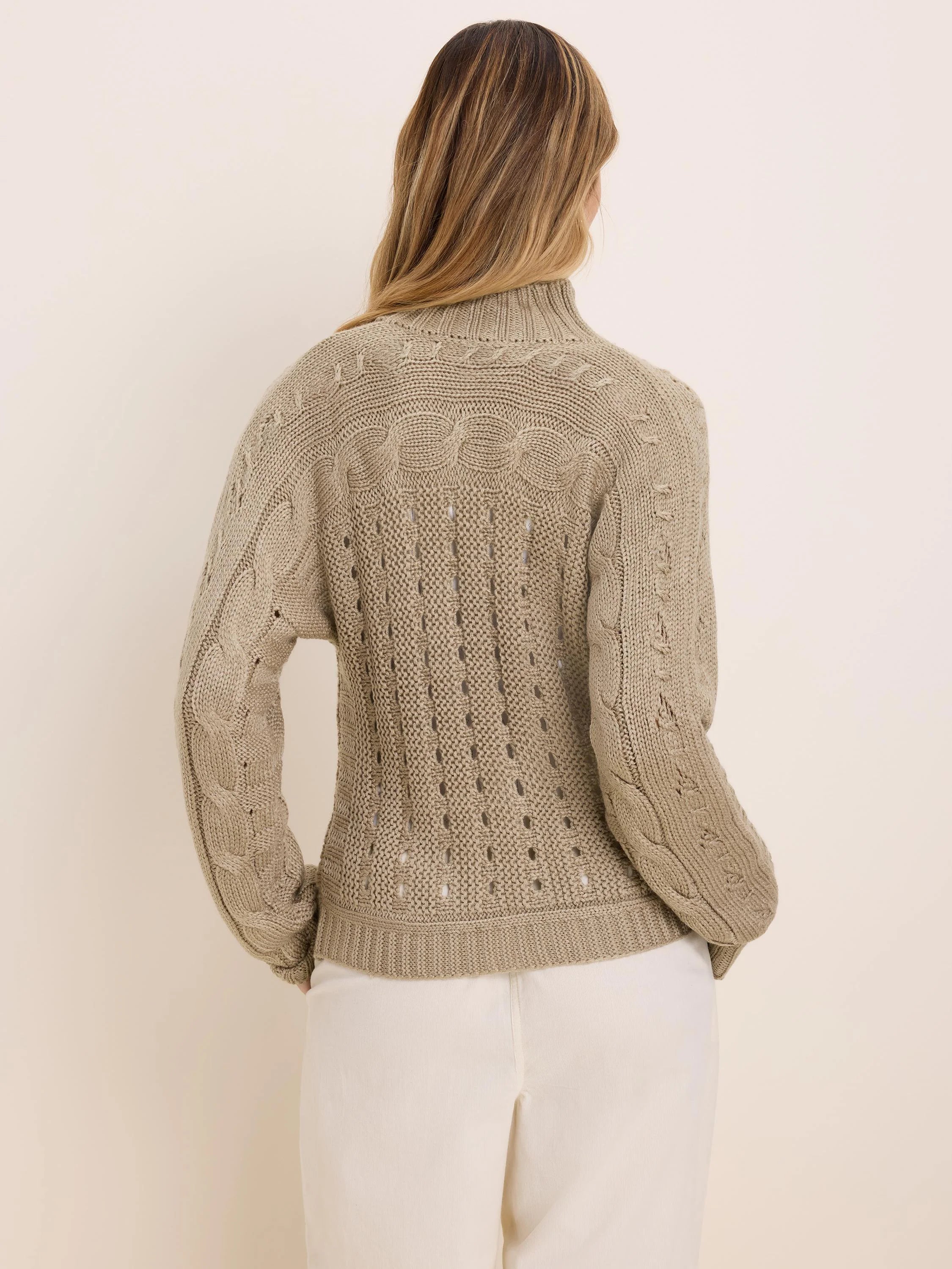 Tan cable knit cardigan on model's back, with cable patterns on sleeves and an openwork design on the back.