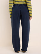 Dark blue relaxed-fit pants with wide straight legs, an elasticated waist, and an unfinished hem. Back view.