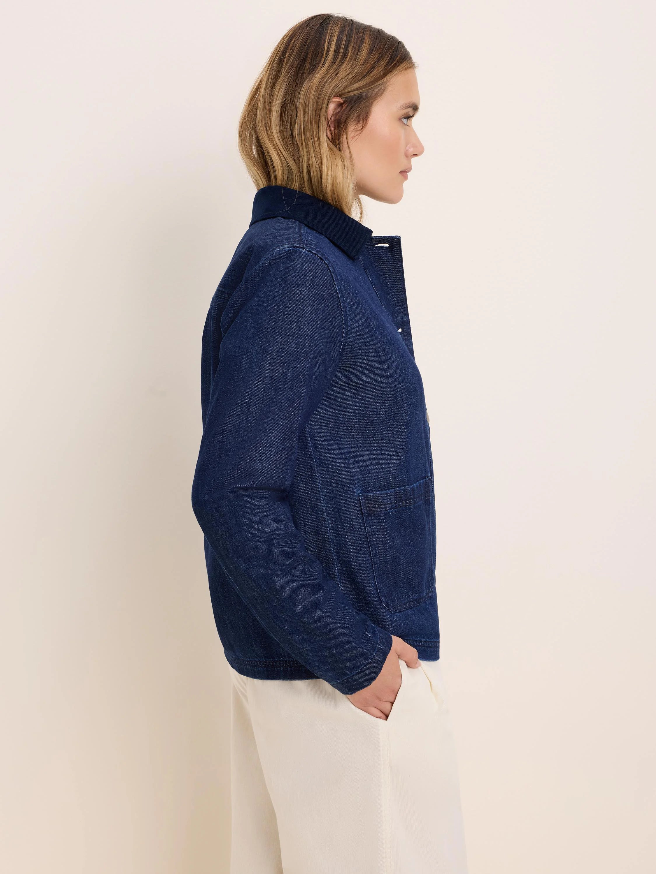Dark indigo denim trucker jacket. It has a ribbed collar, visible buttons, and large front patch pockets.