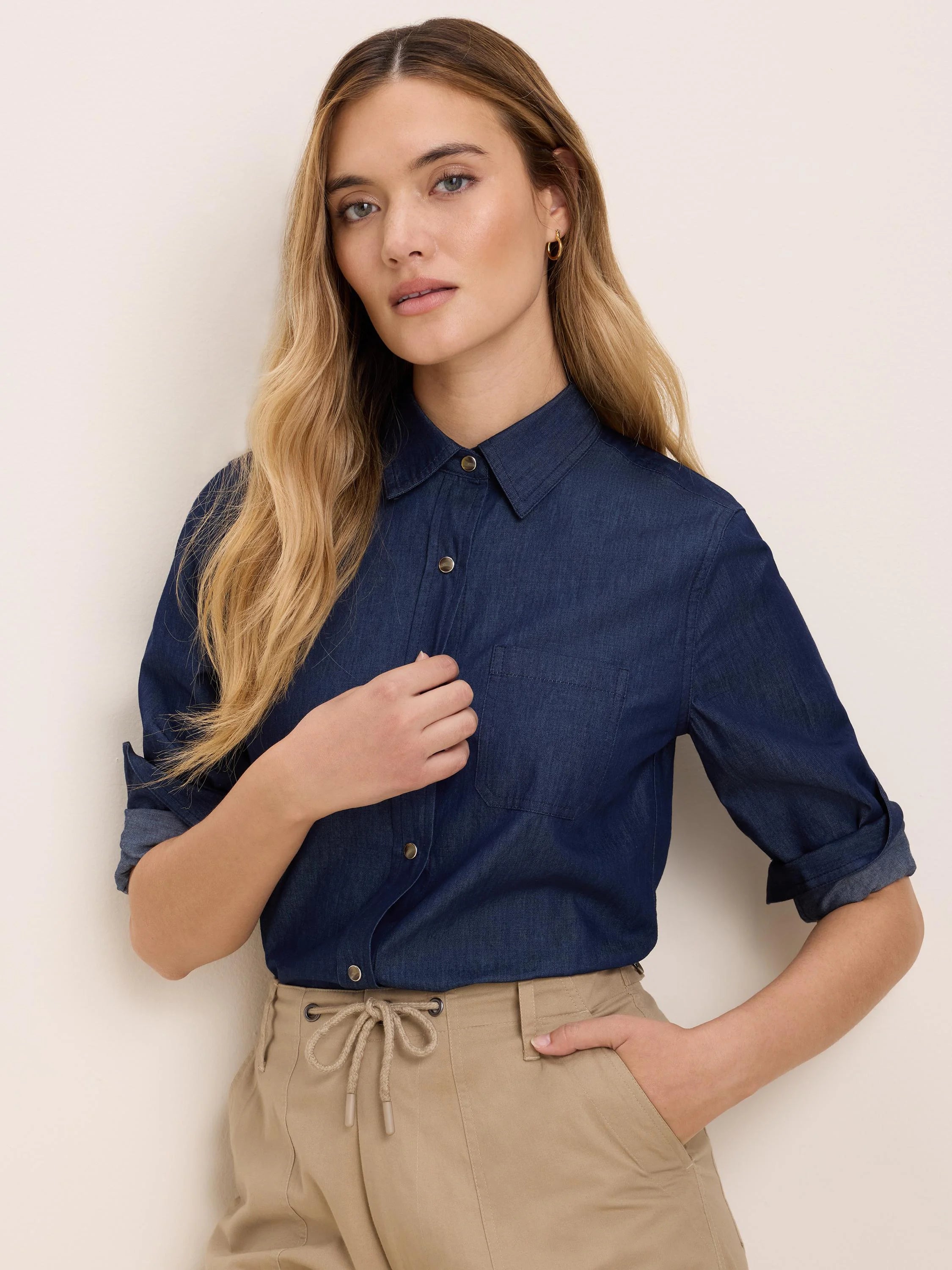 Dark blue collared denim shirt with gold snap buttons, a left chest pocket, and sleeves rolled to 3/4 length.