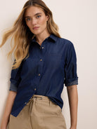 Dark indigo denim shirt with silver snap buttons, a collar, chest pocket, and rolled sleeves.