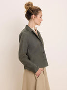 Dark olive green corduroy shirt jacket with vertical ribs, collar, brown buttons, chest pocket, and a cropped length.
