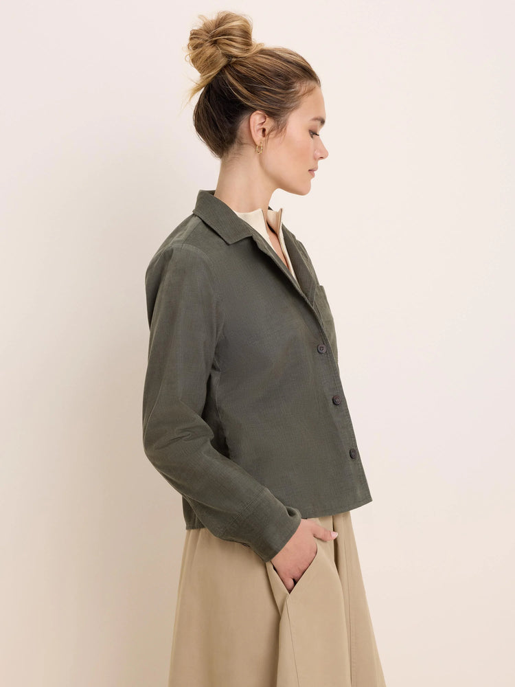 Dark olive green corduroy shirt jacket with vertical ribs, collar, brown buttons, chest pocket, and a cropped length.