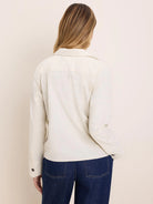 Cream baby corduroy shirt jacket, seen from the back. Features a collar, long sleeves with dark buttoned cuffs, and fine...