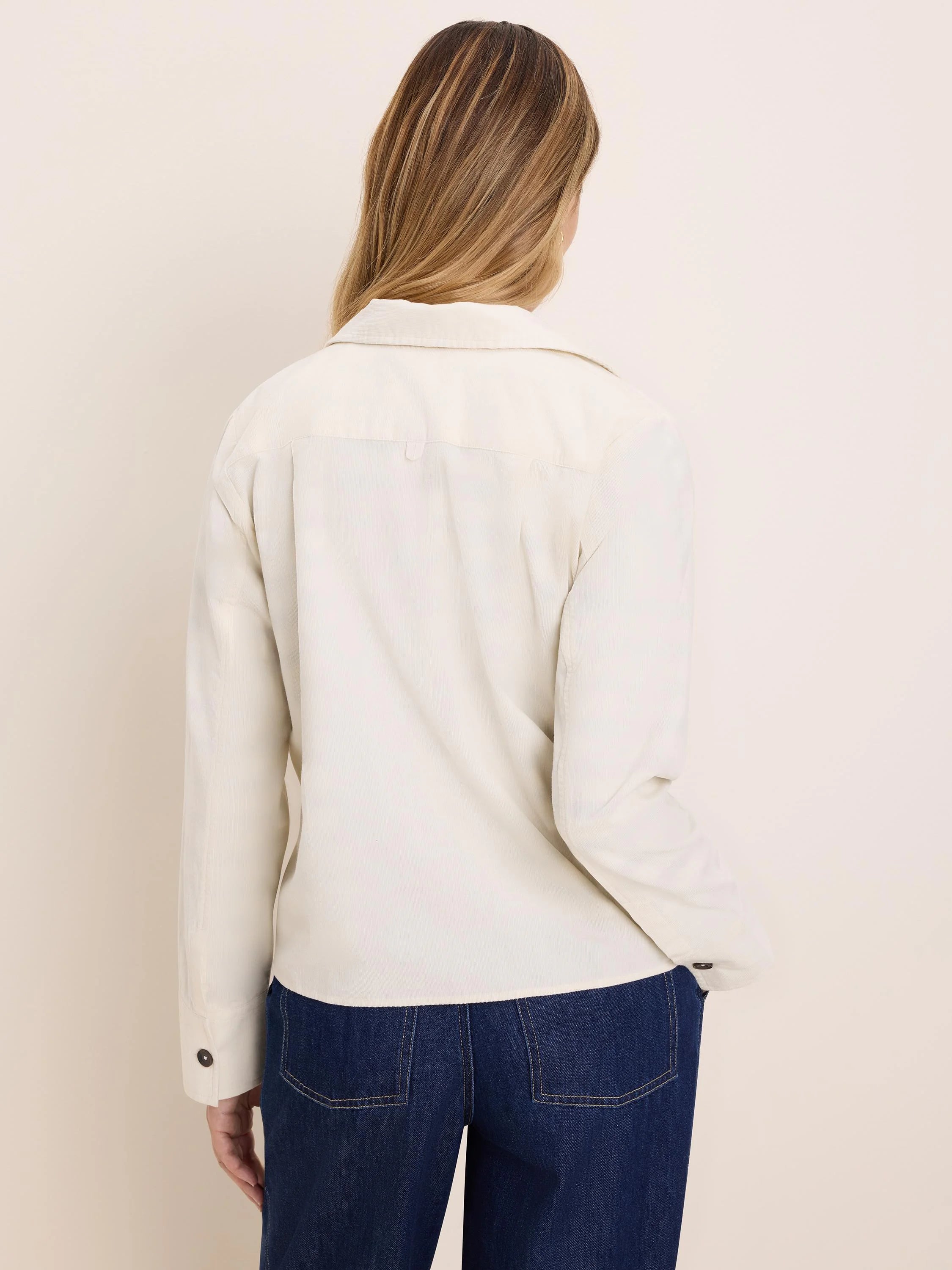 Cream baby corduroy shirt jacket, seen from the back. Features a collar, long sleeves with dark buttoned cuffs, and fine...