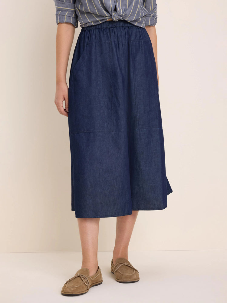 Dark blue denim midi skirt with elastic waist, two front patch pockets, and a drapey A-line shape.