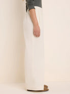 Cream baby cord wide-leg pants with front pleats, shown from the side on a model.